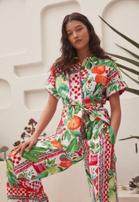 Barvita romper s kratkimi rokavi z motivom cvetja in sadja v rdeči, zeleni in rumeni barvi. Ohlapen kroj s pasom, ki se zaveže v pasu.