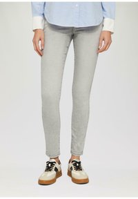 Hellegraue Skinny Jeans aus Denim, kombiniert mit beigen und schwarzen Sneakers mit einer strukturierten Sohle und Schnürdesign.
