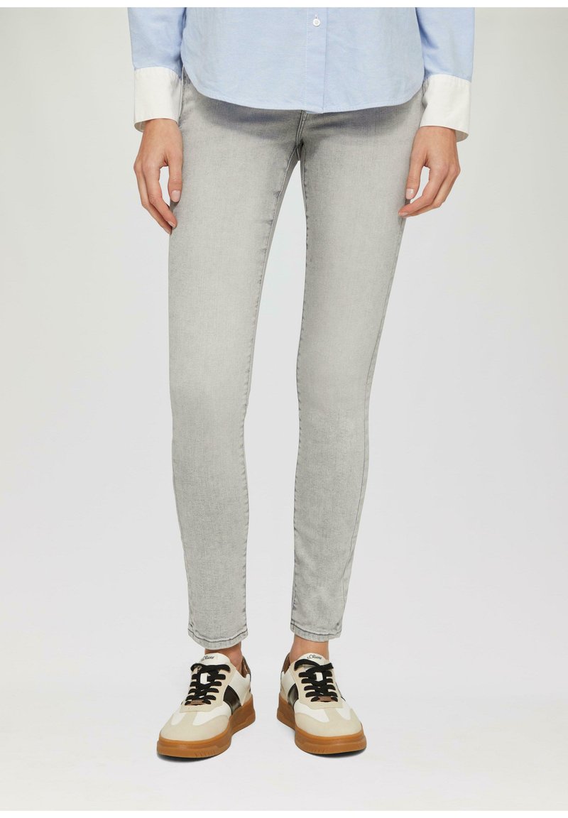 Hellegraue Skinny Jeans aus Denim, kombiniert mit beigen und schwarzen Sneakers mit einer strukturierten Sohle und Schnürdesign.