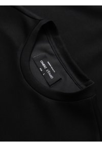 T-shirt noir col rond montrant une étiquette de tissu taille L cousue à l'intérieur du col avec le nom de la marque "OMBRE EXMIO."