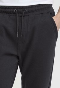 Czarne spodnie dresowe z elastycznym paskiem, sznurkiem do regulacji i bocznymi kieszeniami. Wykonane z miękkiego, teksturowanego materiału. Luźny krój.