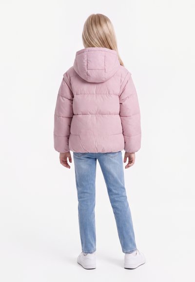 Enfant aux longs cheveux blonds portant une doudoune rose à capuche, un jean bleu clair et des chaussures blanches, debout de dos.