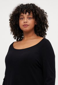 Black long-sleeve top with a wide scoop neckline and textured fabric. The design features subtle seams along the shoulders.