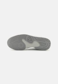 Semelle d'une chaussure de sport grise et blanche avec motifs de traction, logo Jordan près de la voûte plantaire, et logo Nike Air près du talon sur un fond uni.