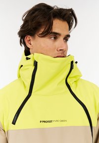 Heldere gele waterdichte jas met een hoge kraag, zwarte ritsen en een beige onderstuk met de branding "PROTEST PVR GREEN".
