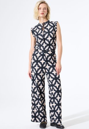 Marinefarbener Jumpsuit mit cremefarbenem geometrischen Muster, ausgestattet mit kurzen Rüschensleeves, einem Schlüssel-Detail vorne und weiten Beinen. Glatte Stofftextur.