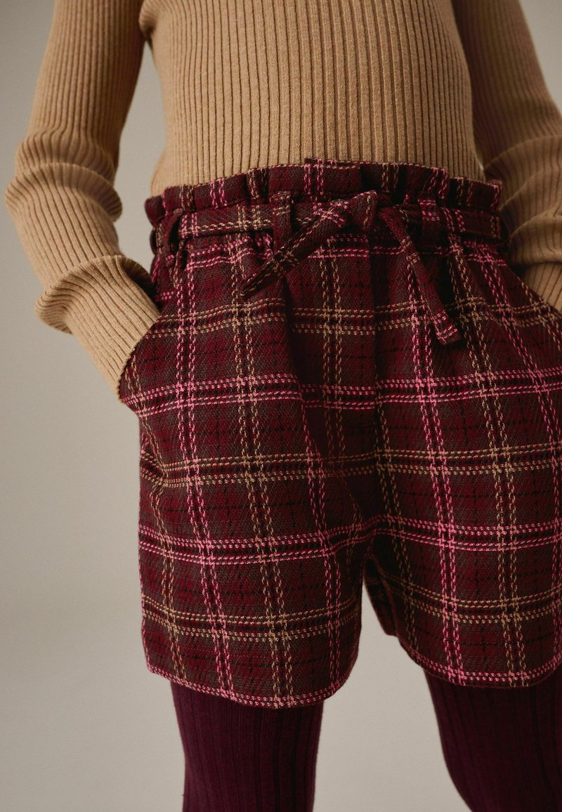 Pantaloni corti a quadri in bordeaux con righe rosa e beige. Presentano una vita arricciata con un laccio e due tasche frontali. Tessuto testurizzato.