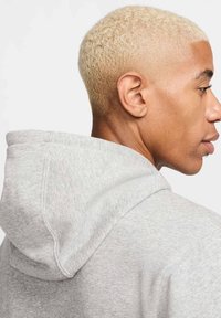 Hoodie harmaa, joka on valmistettu teksturoidusta puuvillasekoitteesta, suurella hupulla ja ompelutiedoilla, kuvattuna sivulta.