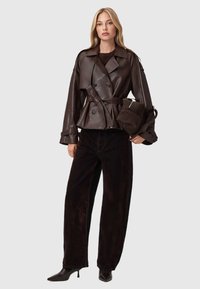 Bruine leren dubbelzijdige jas met een strikceintuur, gecombineerd met een wijde, donkerbruine corduroybroek en puntige zwarte hakken.