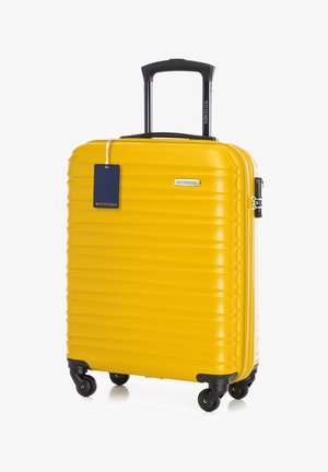 Žlutý kufr s tvrdou skořepinou, vertikálně žebrovaným povrchem, skládacím černým madlem, čtyřmi kolečky a připevněnou modrou značkovou visačkou.