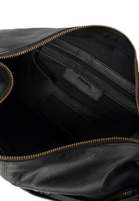 Interno di una borsa nera in pelle con una cerniera, caratterizzato da una fodera in tessuto nero, multiple tasche e un'etichetta in pelle testurizzata. Accenti in cerniera dorati.