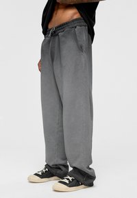 Grijze sweatpants met een elastische tailleband, zijzakken en een relaxte pasvorm. De textuur lijkt zacht en de stof heeft een lichte glans.