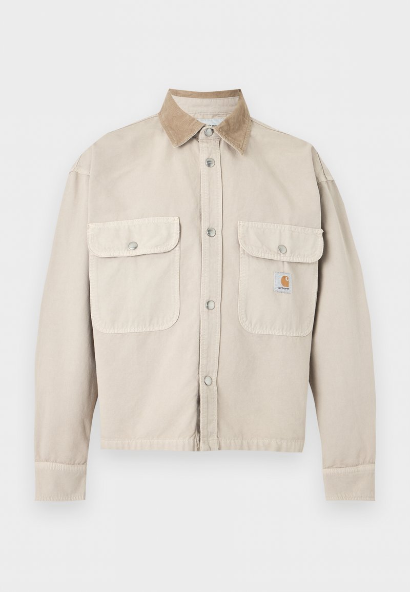 Chaqueta beige con botones, dos bolsillos delanteros con solapa y un cuello de pana marrón claro en contraste, con un pequeño parche de logo en el bolsillo derecho.