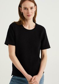 Czarny t-shirt z krótkim rękawem wykonany z teksturowanej dzianiny, z okrągłym dekoltem i luźnym krojem, uzupełniony o detal w postaci bocznego rozcięcia.