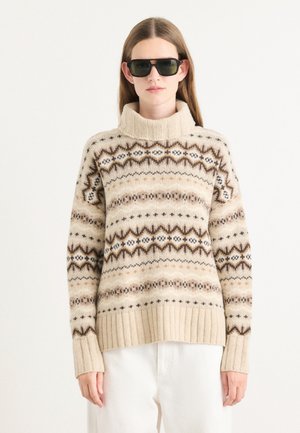 Beige gebreide trui met een hoge nek, geribde mouwen en duidelijke bruine geometrische patronen op een crème achtergrond.
