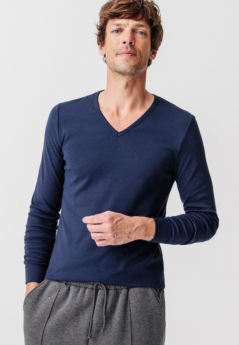T-shirt a maniche lunghe blu navy con scollo a V in tessuto morbido, abbinato a pantaloni della tuta grigi. Presenta una vestibilità comoda e una cucitura discreta lungo il colletto.