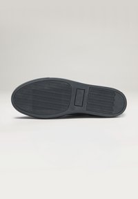 Semelle de chaussure en caoutchouc noir avec un motif texturé ; présente un logo rectangulaire et une indication de taille. Design plat et large avec des bords courbés.