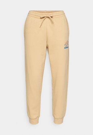 Beige jogger pants made of soft cotton with an elastic waistband, drawstring, and ribbed cuffs. Features a blue and orange logo on the leg.