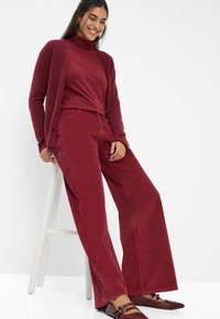Cardigan a maglia borgogna su un dolcevita abbinato, pantaloni in corduroy borgogna a gamba larga e scarpe basse borgogna con dettagli a strap.