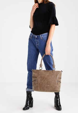 Brun faux læder tote taske med to top håndtag, to front lynlås lommer og en tekstureret overflade, parret med blå jeans og sorte ankelstøvler.