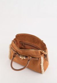 Sac à main en daim beige avec une fermeture éclair sur le dessus, des accents en cuir et des détails en peluche sur les côtés. Il possède des poignées marron et une poche intérieure.