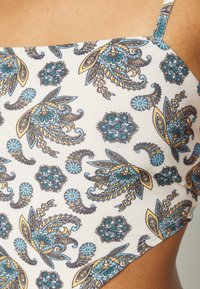 Biquíni com um fundo bege claro e padrões paisley e florais em azul e castanho, alças ajustáveis, textura suave e design justo.