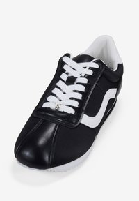 Black and white athletic shoe with a smooth leather and canvas upper, round toe, white laces, and logo detail on the tongue.