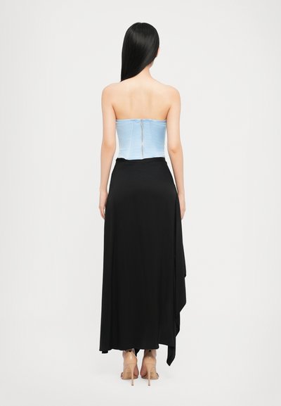 Top corsé sin tirantes de color azul claro con cierre de cremallera, combinado con una falda negra fluida con un dobladillo drapeado. Zapatos de tacón alto transparentes visibles.