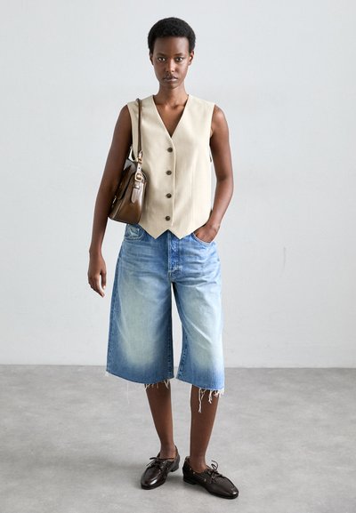 Beige sleeveless vest with four buttons, paired with light blue denim culottes with frayed hems and brown leather shoes. Brown handbag.
