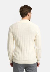 Maglione a coste crema con colletto sciallato, caratterizzato da una superficie texturizzata, maniche lunghe e orlo aderente.