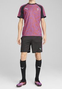 Sportowy strój Puma z falistym wzorem w fiolecie i czerwieni, czarne spodenki, czarne skarpetki do kolan z odblaskowymi detalami i logo.