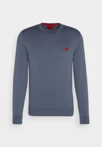 Pull à manches longues col rond en bleu ardoise avec un petit patch logo rouge sur la poitrine et des poignets et un ourlet côtelés.