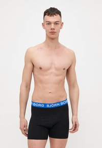 Black boxer shorts with a blue "BJÖRN BORG" waistband. The material appears smooth and stretchy, fitting snugly on the body.
