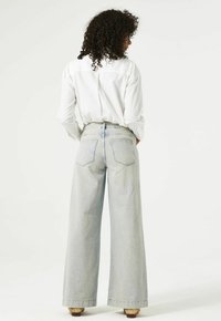 Lichtblauwe high-waisted wijde jeans met een rafelige zoom, twee achterzakken en een relaxte fit, gecombineerd met een wit knoopshirt.