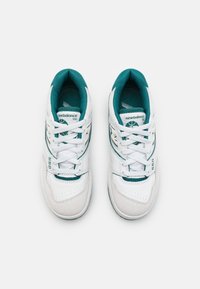 Baskets blanches avec des accents turquoise, présentant une tige en cuir et suède, un système de laçage, et une boîte à orteils perforée. Numéro de modèle 550 sur le côté.