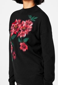 Svart tröja med livfulla, broderade röda och rosa blommor med gröna blad. Rund hals, långa ärmar och avslappnad passform.