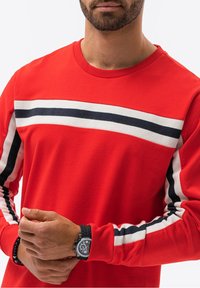Sudadera de manga larga roja de algodón, con rayas horizontales blancas y marinas en las mangas y el pecho. Cuello y puños acanalados.