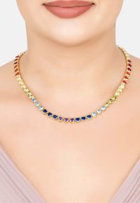 Choker necklace with heart-shaped gemstones in a gradient of colors worn on a woman's neck with nude lipstick and light purple top.
