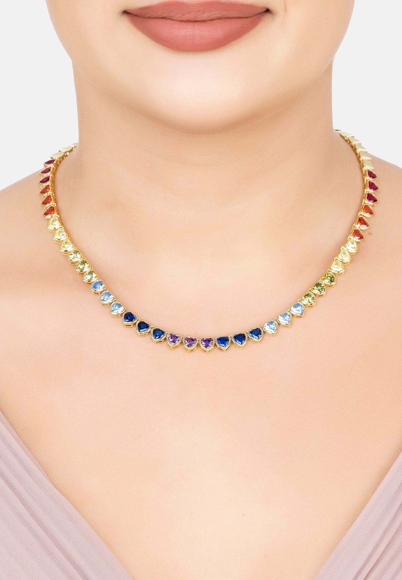 Choker necklace with heart-shaped gemstones in a gradient of colors worn on a woman's neck with nude lipstick and light purple top.