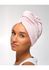 Rosa frottéhåndkle viklet rundt hodet, som viser en myk tekstur. Håndkleet er vridd og lagdelt, holdt på plass uten synlige festemidler.