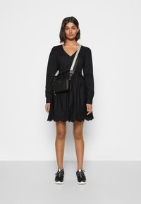 Vestido preto com mangas longas, decote em V e bainha com bordado em flores, combinado com uma pequena bolsa preta de ombro e sapatilhas.