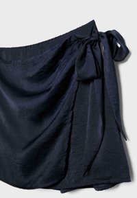 Jupe portefeuille bleu marine foncé avec un nœud de côté et un tissu doux légèrement texturé sur un fond uni.
