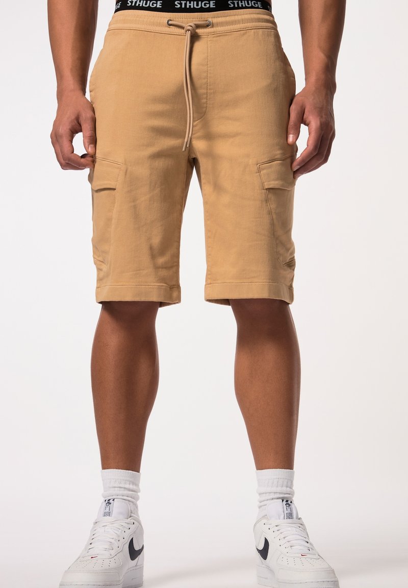 Shorts cargo beiges avec des ourlets retroussés, deux poches latérales et une taille à cordon. Portés avec des baskets blanches et des chaussettes de mi-mollet.