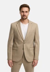 Beige Sakko mit zwei Knöpfen, Reverskragen und seitlichen Taschen. Aus glattem Stoff, kombiniert mit einem weißen Rundhals-T-Shirt.