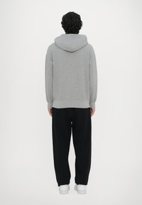 Grauer Kapuzenpullover mit lockerer Passform, gerippten Bündchen und Saum, kombiniert mit schwarzen Jogginghosen und weißen Sneakers, von hinten betrachtet.