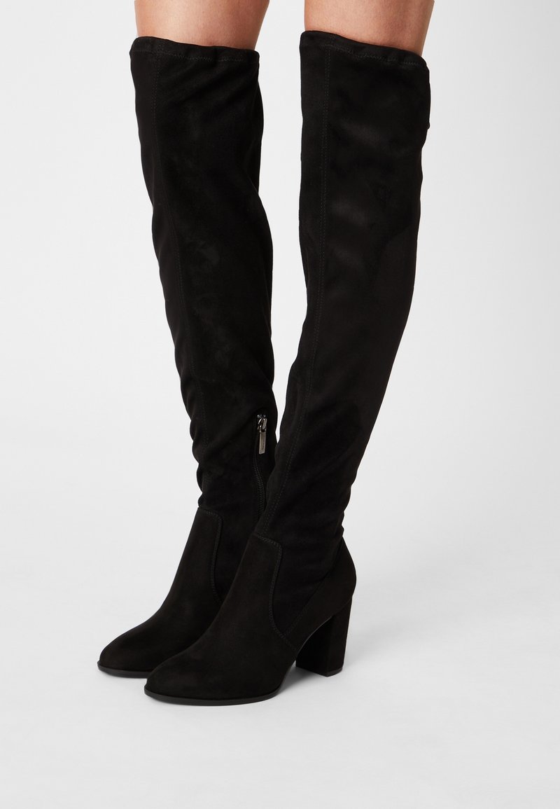Černé semišové kozačky nad kolena s špičatou špičkou a robustním blokovým podpatkem. Mají boční zip a hladký povrch.