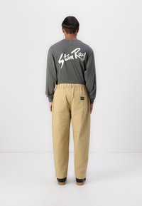 Long-sleeve gray shirt with white logo on back, paired with loose-fitting beige pants, featuring an elastic waistband and side pockets.
