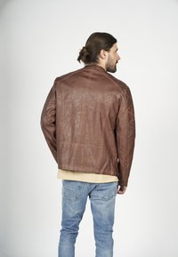 Brun läderjacka med kviltade detaljer, med ståkrage och sidodragkedjor. Bärs över en beige topp och ihop med blå jeans.