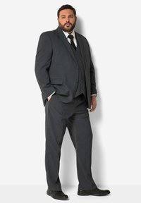 Completo scuro grigio a tre pezzi con revers a punta, giacca monopetto e pantaloni con frontale piatto. Scarpe eleganti nere completano l'outfit.