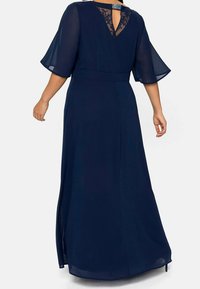 Mörkblå maxiklänning med genomskinliga ärmar med klockform och snörning bak. Har en åtsittande midja och sidofåror för bättre rörelsefrihet.